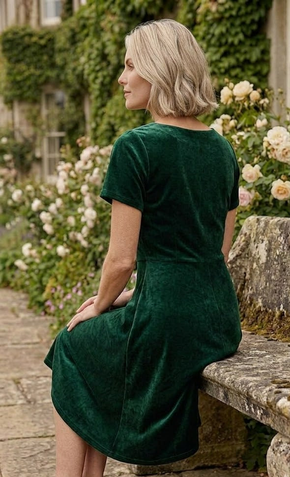 Woman in a green velvet dress sitting on a stone bench in a garden.