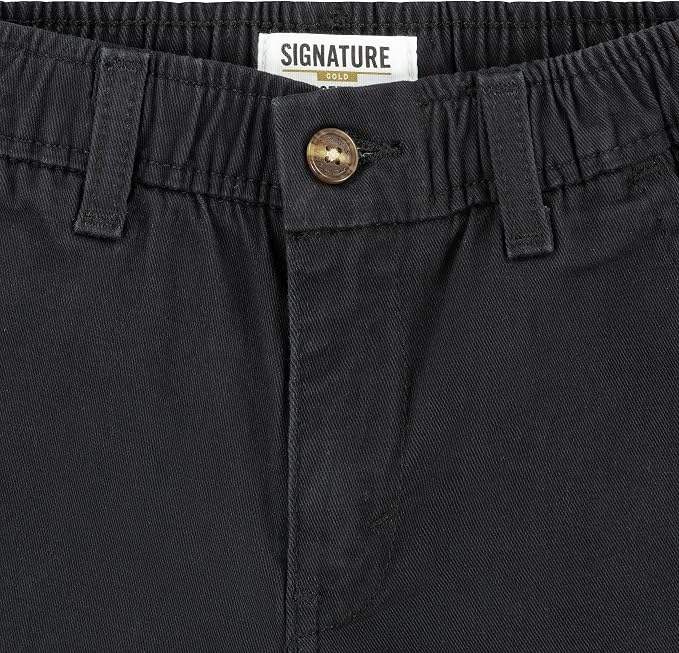 Close-up of black pants showing the waistband, belt loops, button closure, and a white interior label that reads SIGNATURE with a small gold logo.