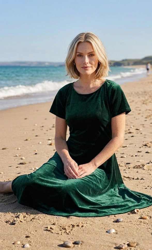 Woman in a green dress sitting on a beach with ocean waves in the background