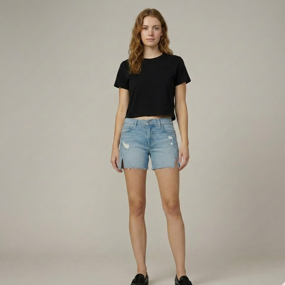 Woman wearing a black t-shirt and light blue denim shorts on a plain background