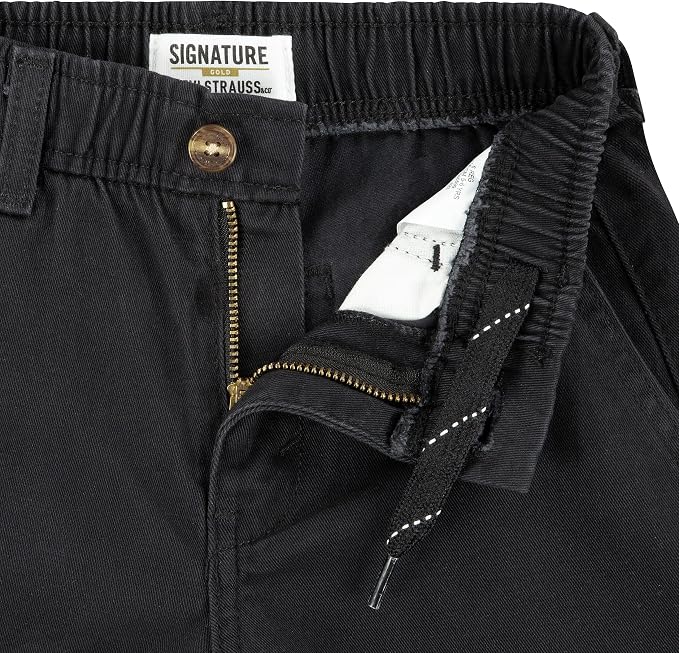 Close-up of black pants showing the waistband, button closure, gold-tone zipper, drawstring detail, and interior white lining. The waistband label reads Signature by Strauss.